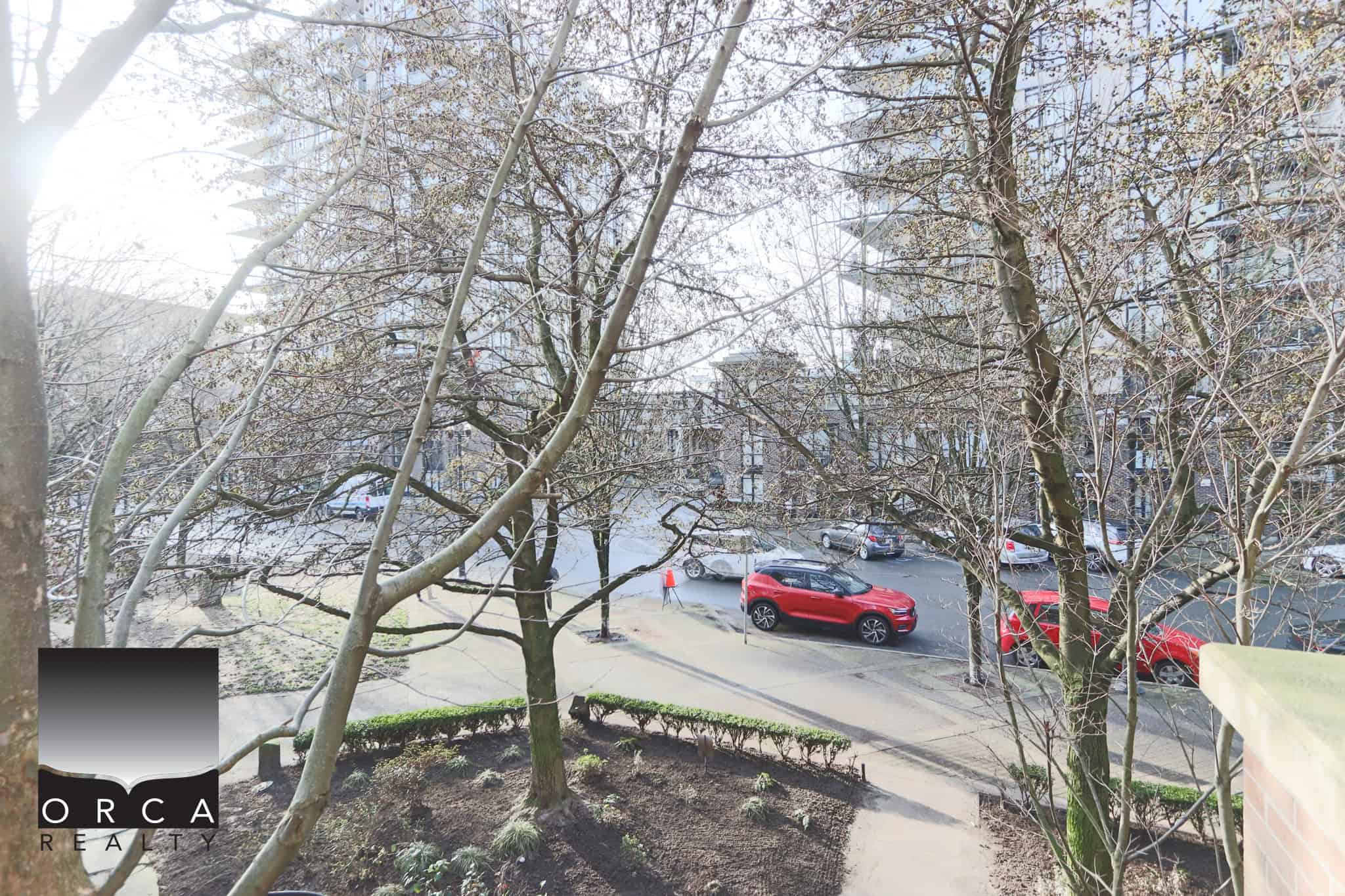 Spacious outdoor view of trees and parking area at 203-170 W 1st Street, North Vancouver, showcasing the neighborhood's natural beauty and convenient location.