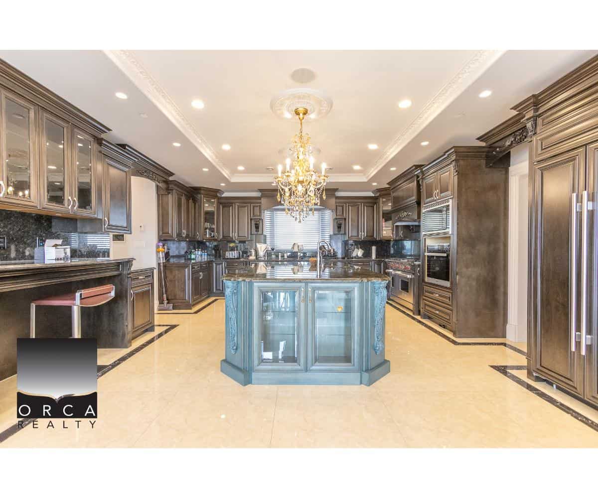 Luxurious modern kitchen with custom dark wood cabinets, granite countertops, a central blue island, and elegant chandelier lighting, perfect for upscale homes.