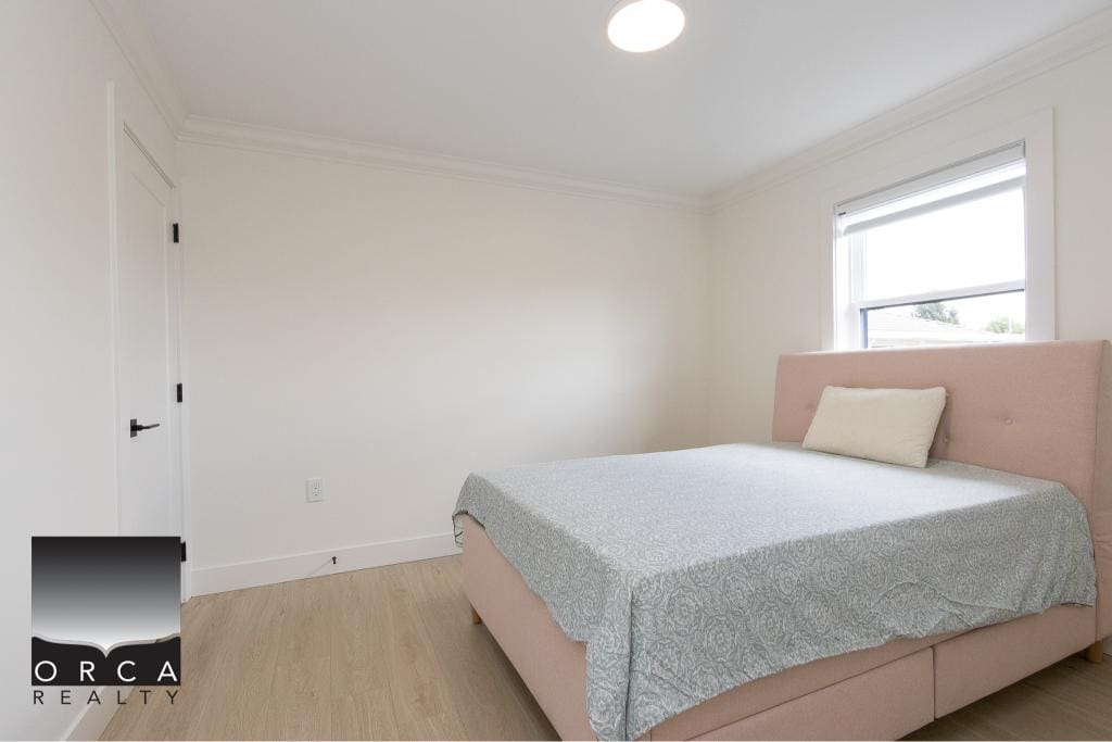 Bright bedroom with white walls, large window, and modern decor, showcasing Orca Realty Inc.'s property listings, ideal for homebuyers seeking comfortable, stylish real estate options in the Vancouver area.