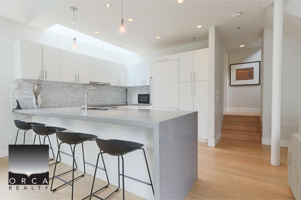 Modern minimalist kitchen with sleek white cabinetry, a large island with seating, stainless steel sink, and contemporary decor, perfect for Vancouver real estate listings.