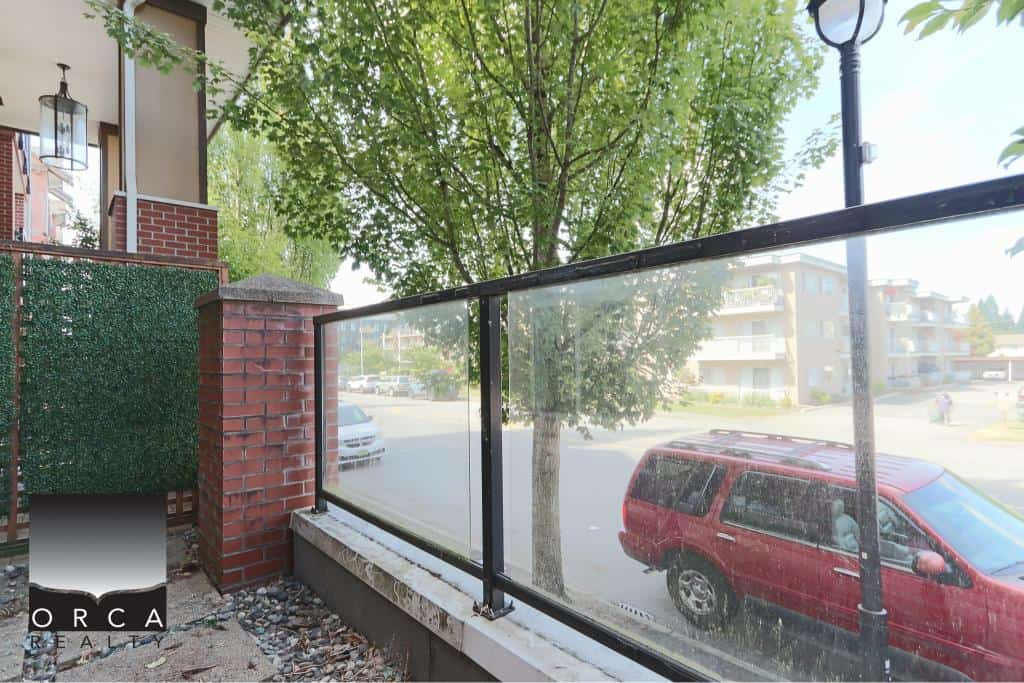Bright outdoor balcony space with glass railing, city views, lush green trees, and modern residential buildings in the background, ideal for relaxing or outdoor activities.