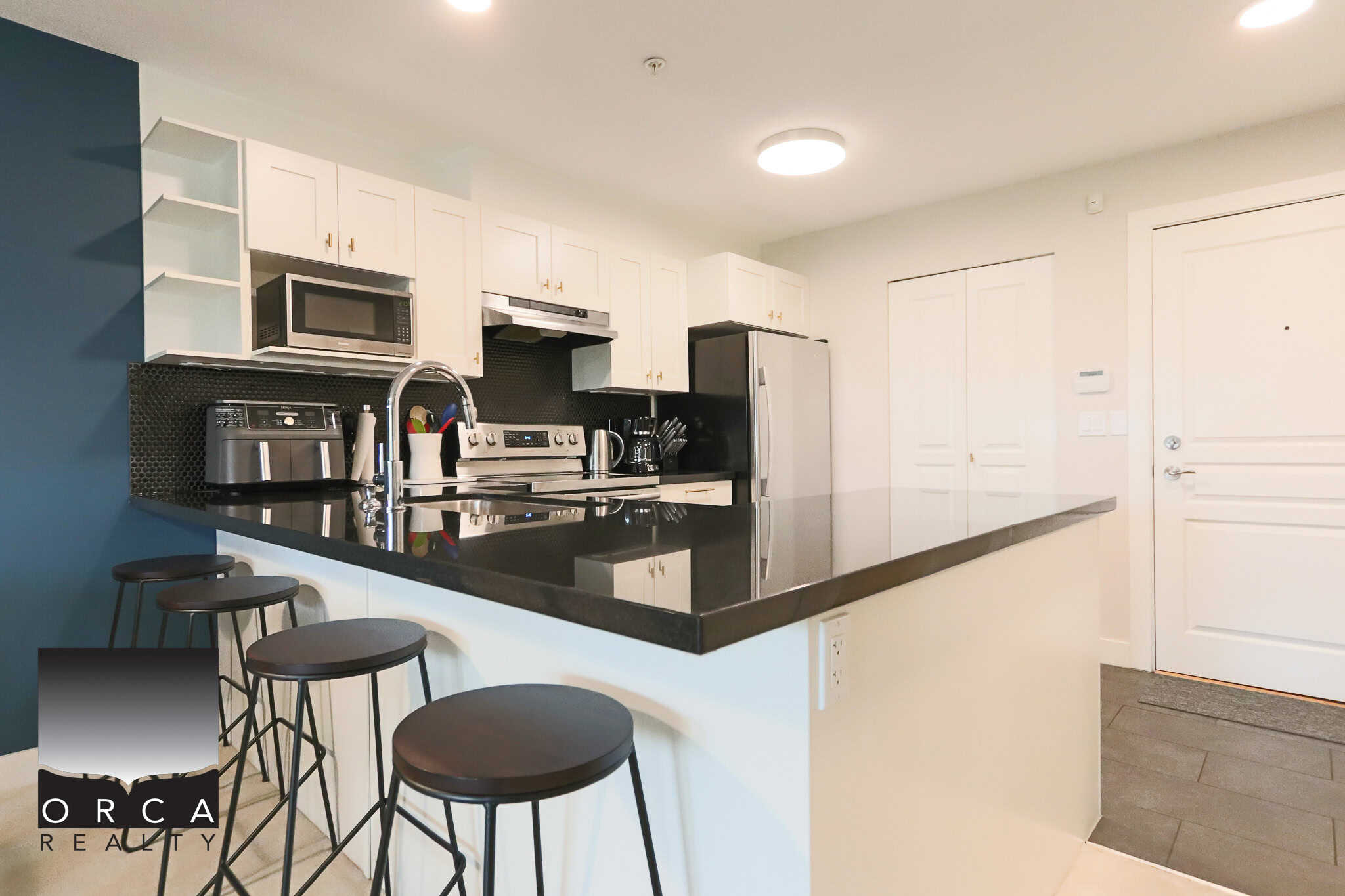 Modern U-shaped kitchen with black countertops and white cabinetry, stainless steel appliances, and a breakfast bar with black stools, ideal for contemporary Vancouver Island living.