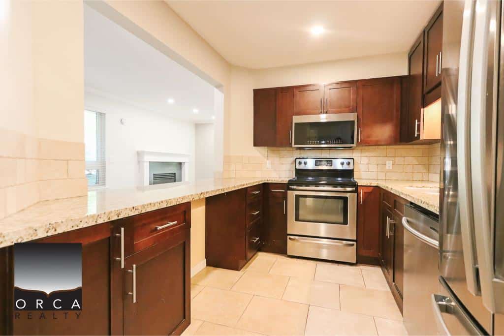 Stainless steel appliances in a modern kitchen with rich wood cabinets and granite countertops, perfect for Vancouver Island real estate buyers.