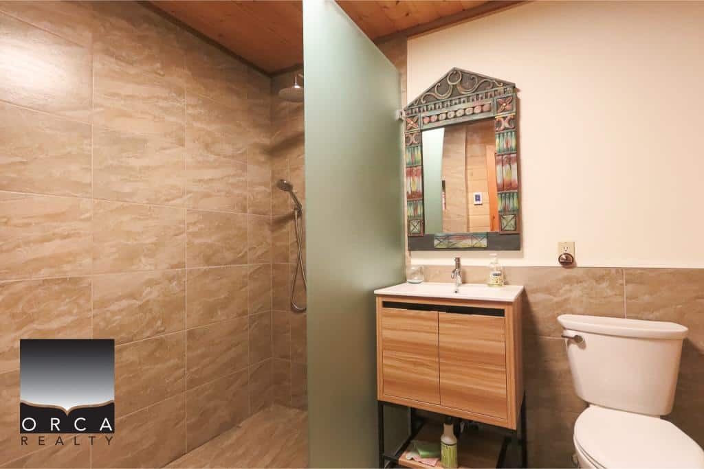 Modern bathroom with a glass-enclosed shower, wooden vanity, and decorative mirror, perfect for Vancouver-area homes. Stylish and functional space showcased by Orca Realty Inc.