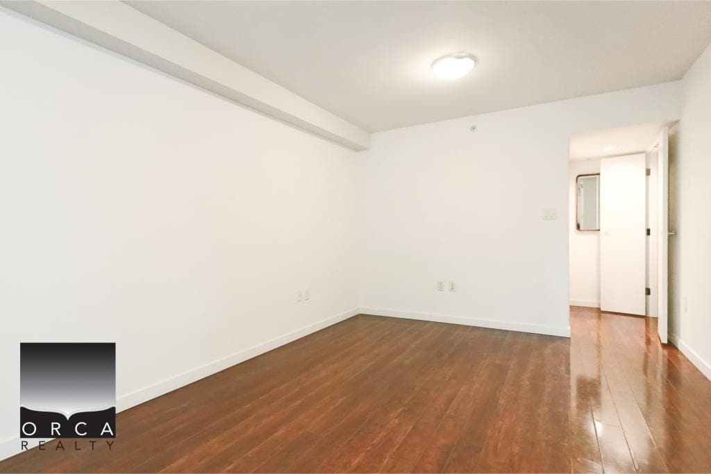 Bright, empty living room with hardwood floors and white walls for rent or sale in Vancouver, BC, by Orca Realty Inc.
