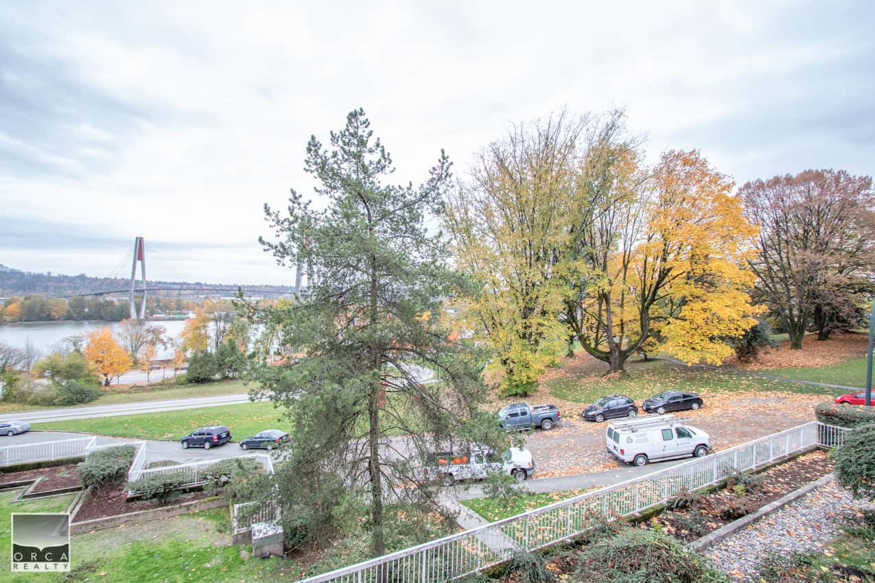 Yellow and green autumn trees overlooking a river with parked cars and a bridge in the background, showcasing scenic views for real estate in Ottawa.