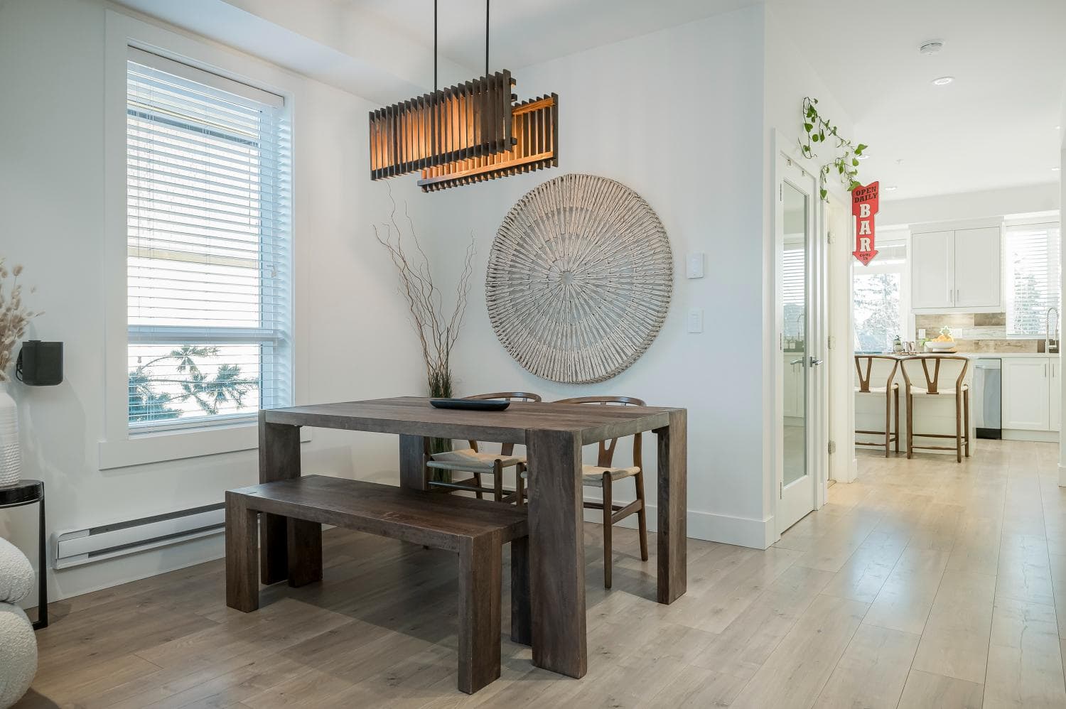 Modern dining area with wooden table and bench, natural light, ocean view, and coastal-inspired decor in a trendy Orca Realty Inc. listing in Canada.