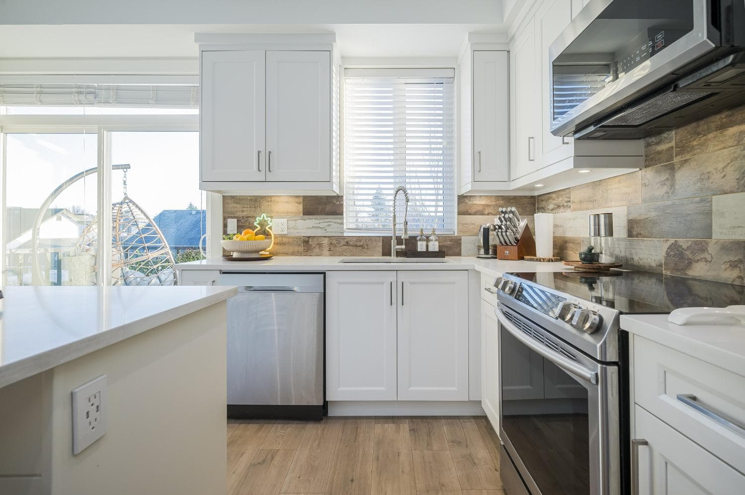Bright modern white kitchen with stainless steel appliances, natural light, and stylish wood backsplash, perfect for Vancouver Island residential real estate and homebuyers.