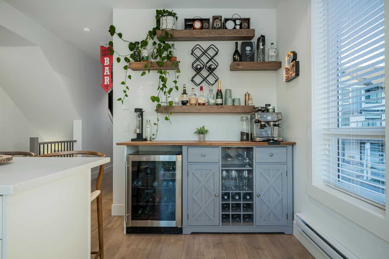 Stylish home bar with wooden shelves and wine storage, featuring a modern coffee machine, wine bottles, and decorative accents in a bright, airy kitchen space.