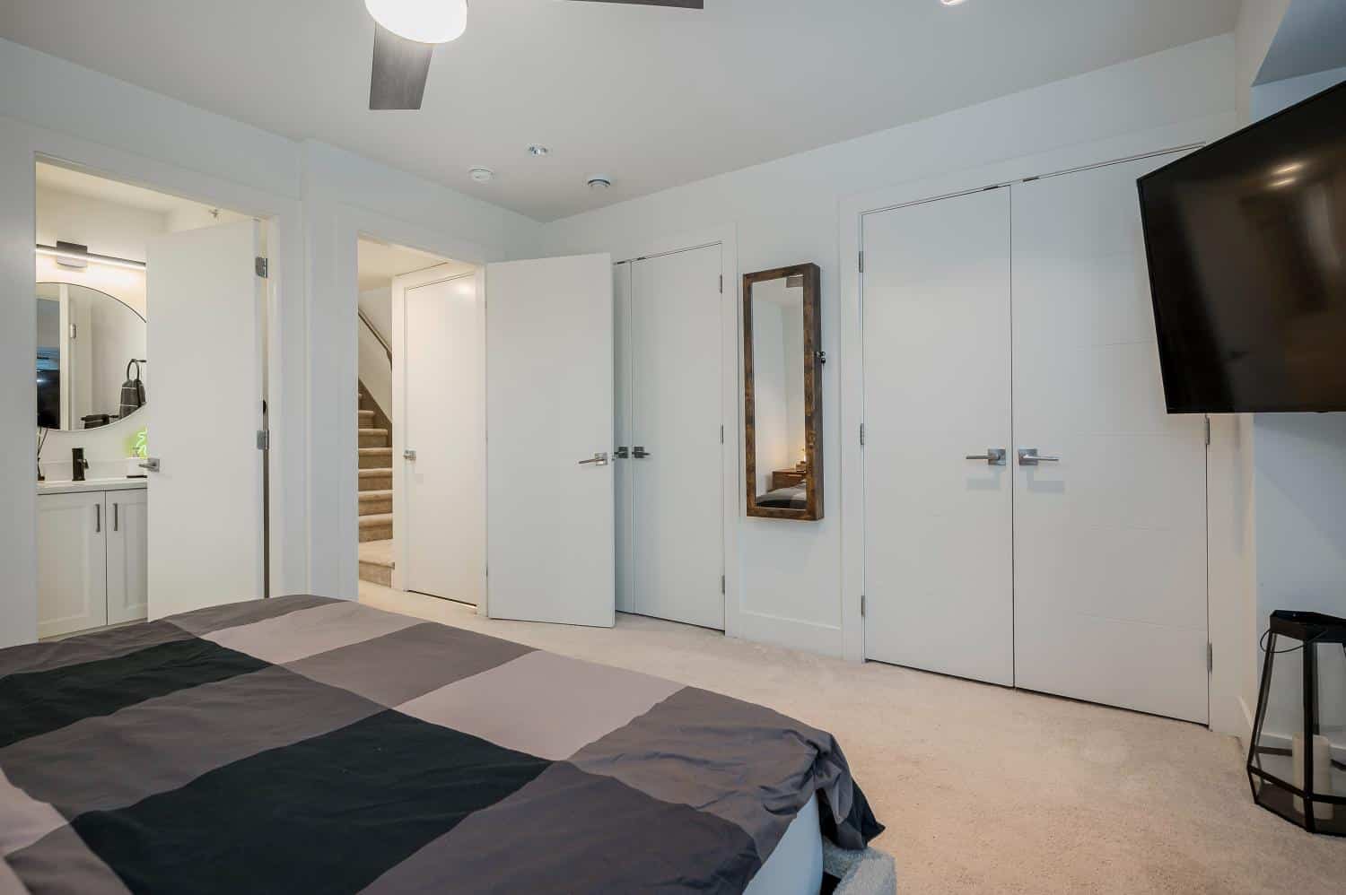 Modern bedroom with white walls, built-in closets, wall-mounted TV, and a full bathroom vanity in the corner, showcasing contemporary home interior design.