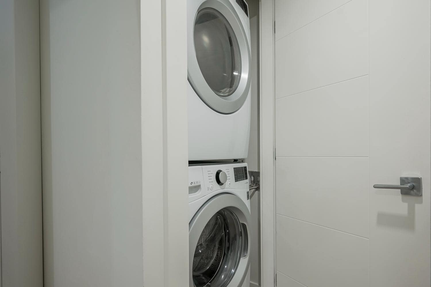 Modern white stacked washer and dryer in a compact laundry closet, ideal for Vancouver homes or condos, showcasing efficient laundry solutions by Orca Realty Inc.