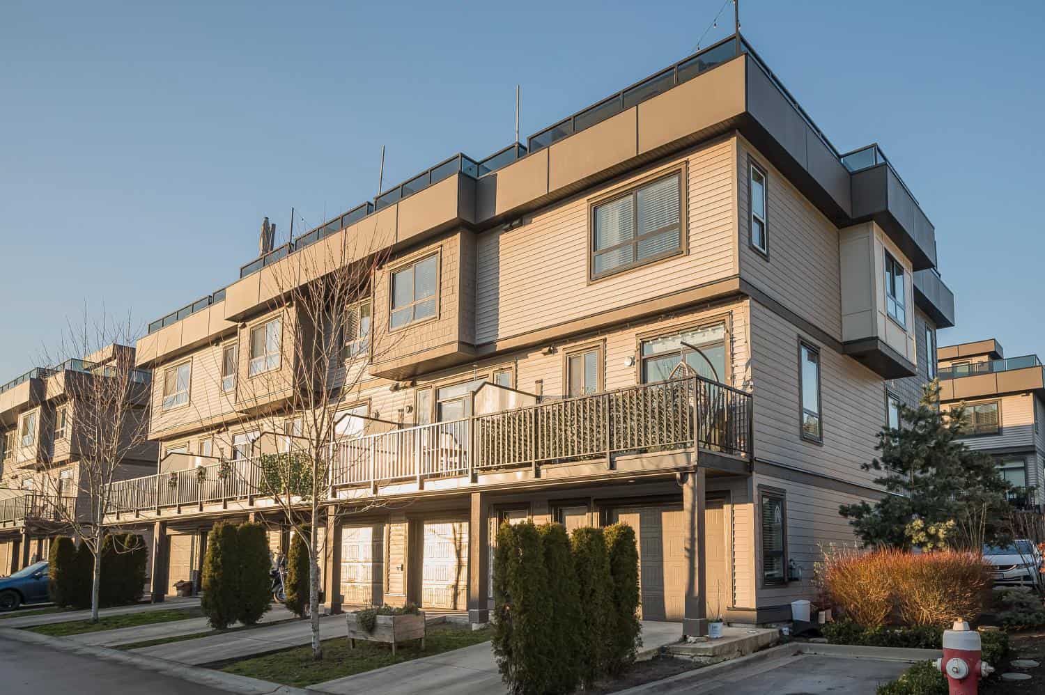 Modern multi-story residential building with spacious balconies, surrounded by landscaped gardens and trees, showcasing contemporary architecture in a scenic neighbourhood.