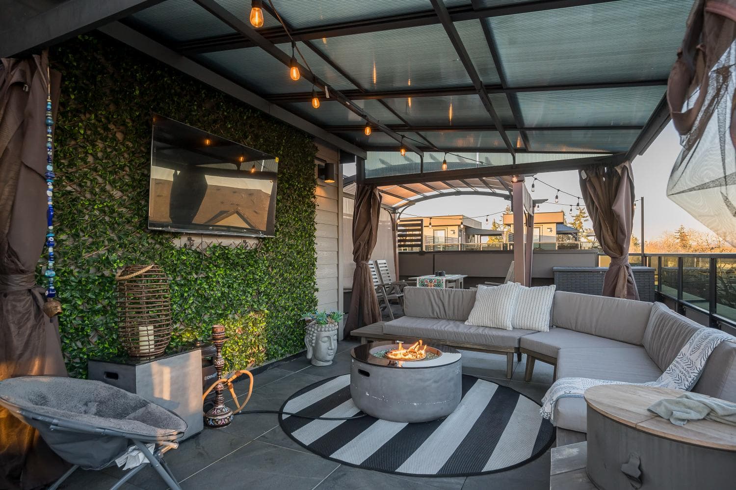 Cozy outdoor patio with modern sectional sofa, fire pit, greenery wall, and string lighting, perfect for Vancouver area home entertaining.