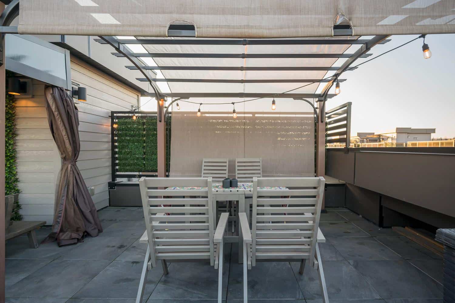 Modern rooftop balcony with outdoor dining area, string lights, and privacy screens, perfect for Vancouver real estate.