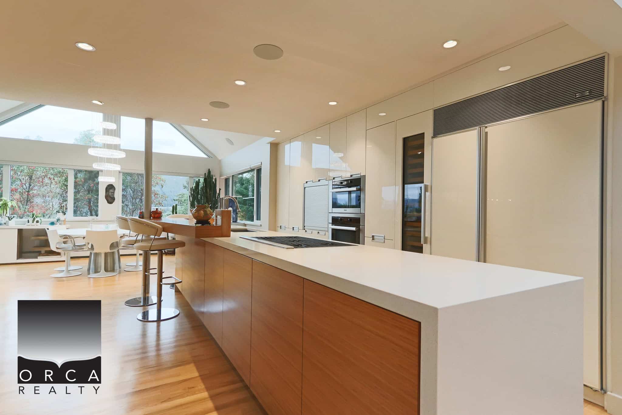 Sleek modern kitchen with built-in appliances, large windows, and minimalist design in a luxury home by Orca Realty Inc.