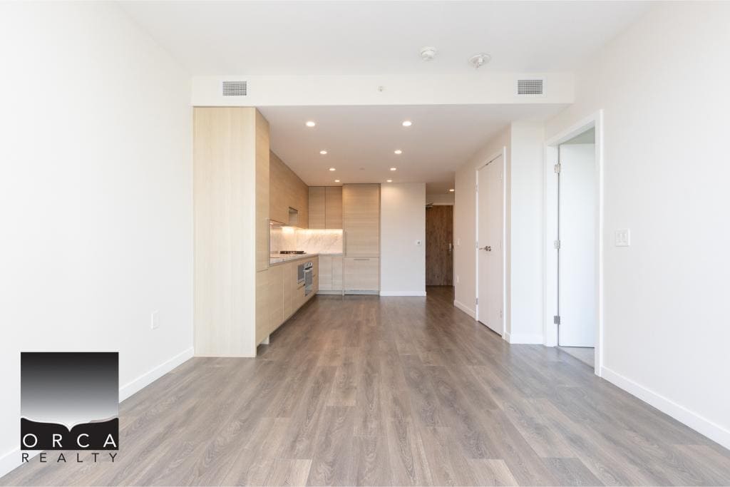 Bright, modern open-concept kitchen and living space in a new Calgary apartment, featuring sleek wood cabinetry, hardwood floors, and ample natural light — perfect for contemporary urban living.