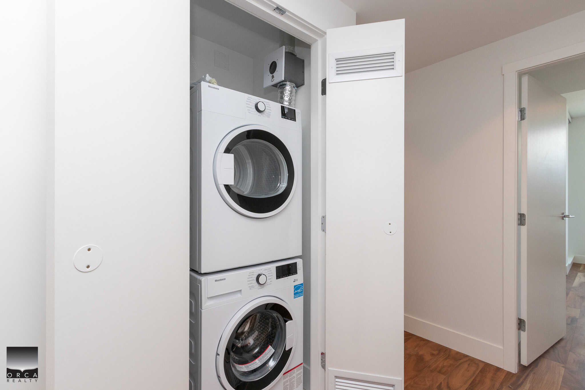 Stacked washer and dryer in a laundry closet, modern appliances with white cabinetry, ideal for Vancouver homes, showcasing convenient laundry solutions from Orca Realty Inc.
