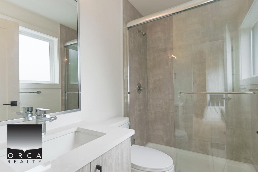Modern bathroom with glass shower and neutral-toned tiles, featuring a sleek white vanity and mirror, ideal for contemporary Vancouver Island homes.
