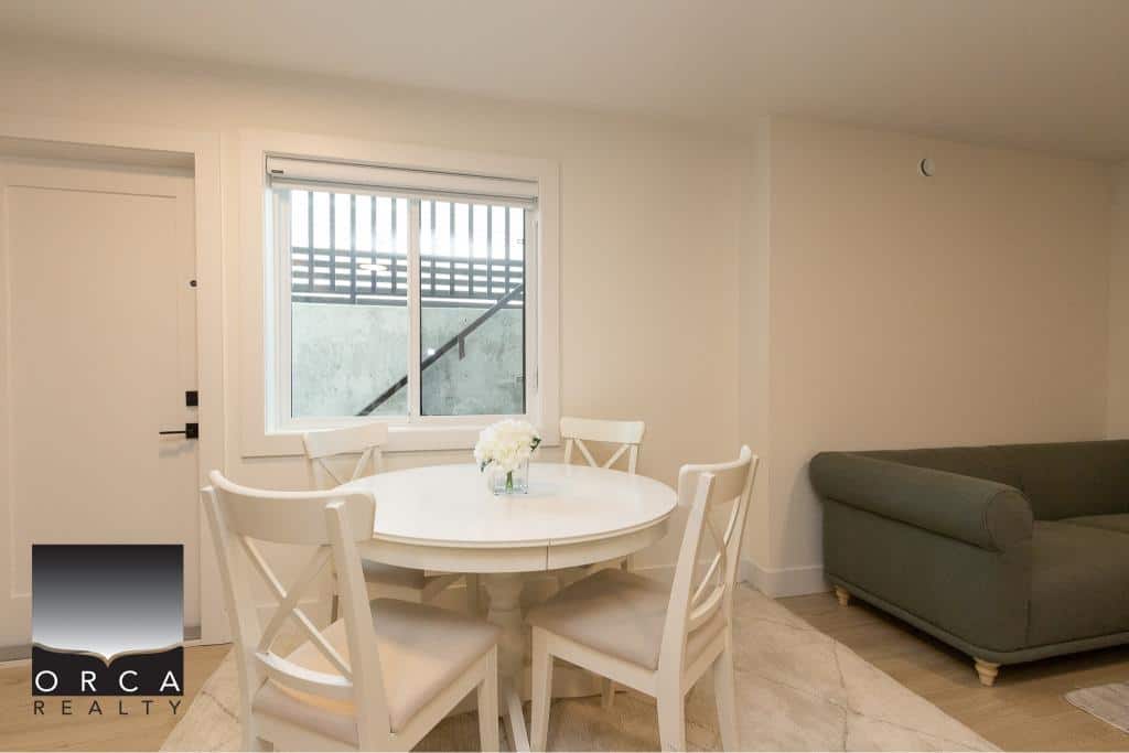 Bright interior of a modern home with a round dining table, white chairs, and a cozy sofa, showcasing Orca Realty Inc. real estate services for Vancouver Island and the surrounding areas.