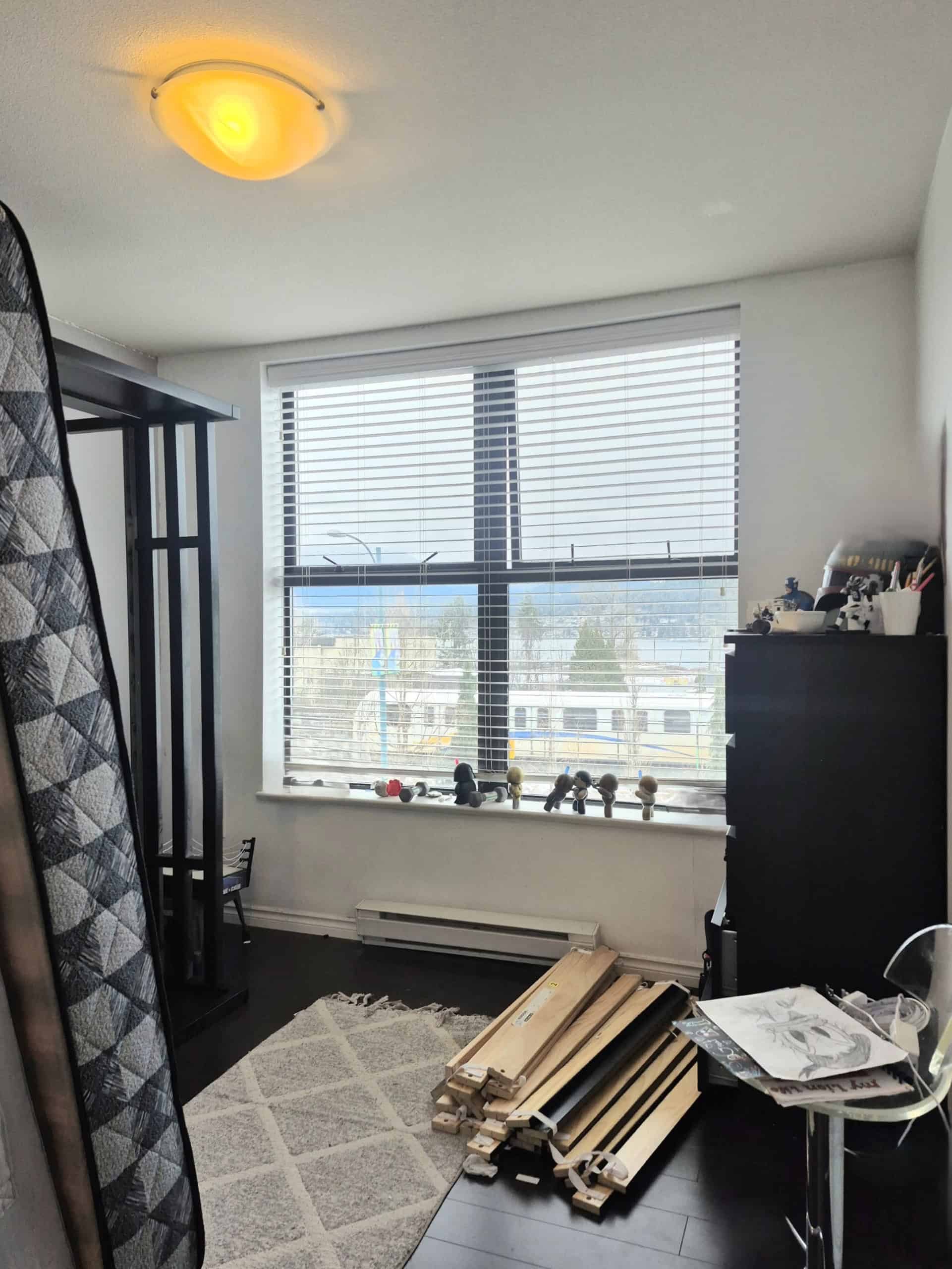 Modern residential interior with large window, blinds, black furniture, and wooden flooring, showcasing a cozy space, ideal for real estate listings or property tours in Vancouver or nearby areas.