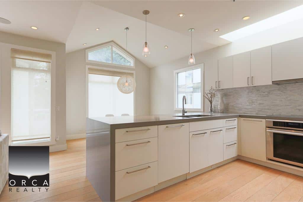 Modern open-concept kitchen with natural light, white cabinetry, stainless steel appliances, and a stylish mosaic backsplash, ideal for Vancouver real estate listings.