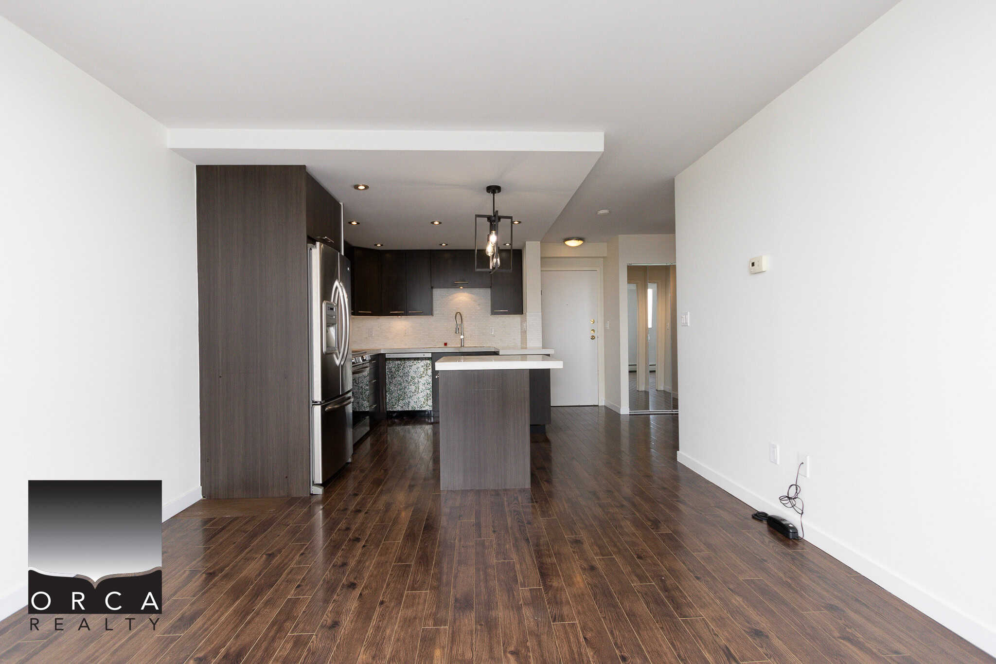 Modern open-concept kitchen with dark wood cabinetry, stainless steel appliances, and a central island in a contemporary condo.