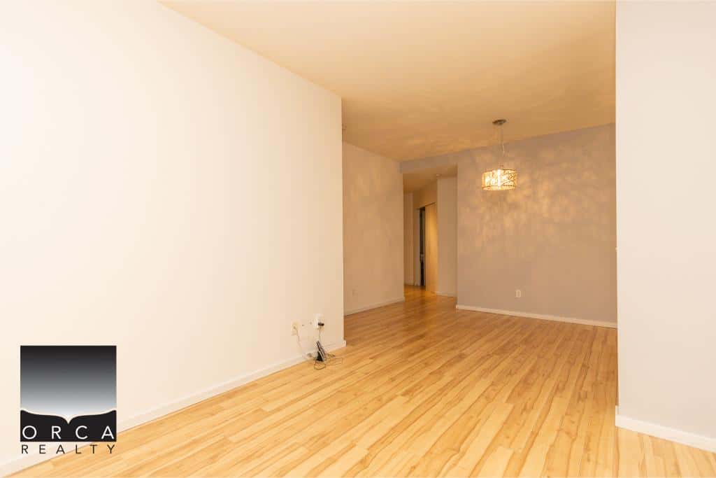 Bright, spacious living room with hardwood flooring and neutral walls, ideal for family gatherings and entertaining; part of a modern property listed by Orca Realty Inc.