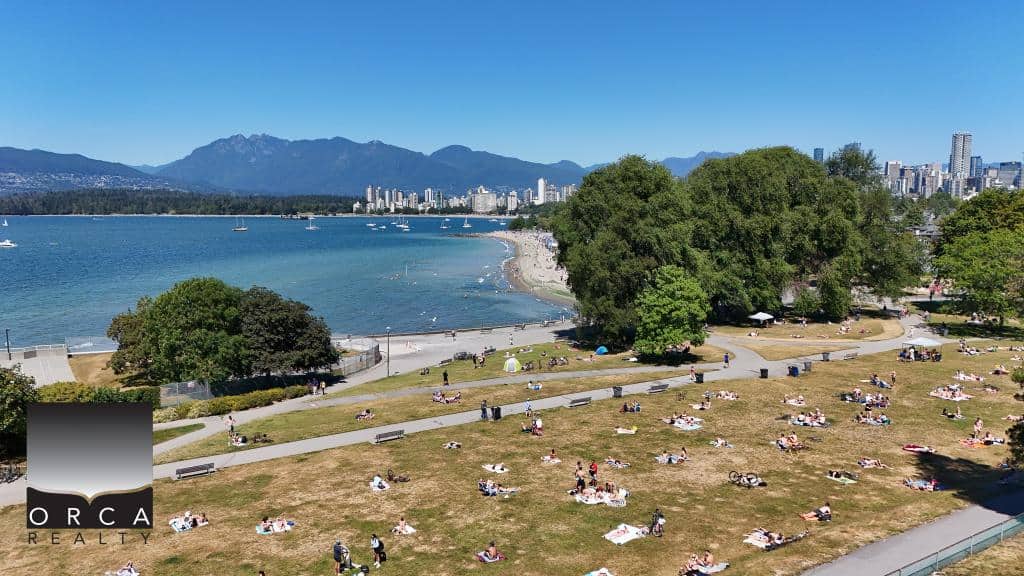 Lively park scene by the water with people relaxing on the grass, scenic city skyline, and mountains in the background, showcasing Vancouver's outdoor lifestyle and real estate opportunities in the area.