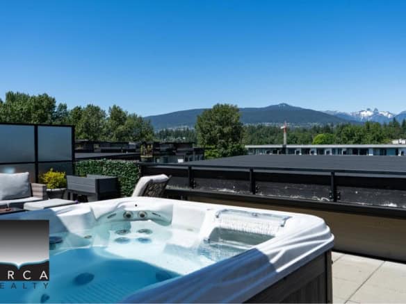 Panoramic rooftop balcony with hot tub and outdoor seating, overlooking lush greenery and distant mountains, ideal for luxury condo living and scenic Vancouver Island views.