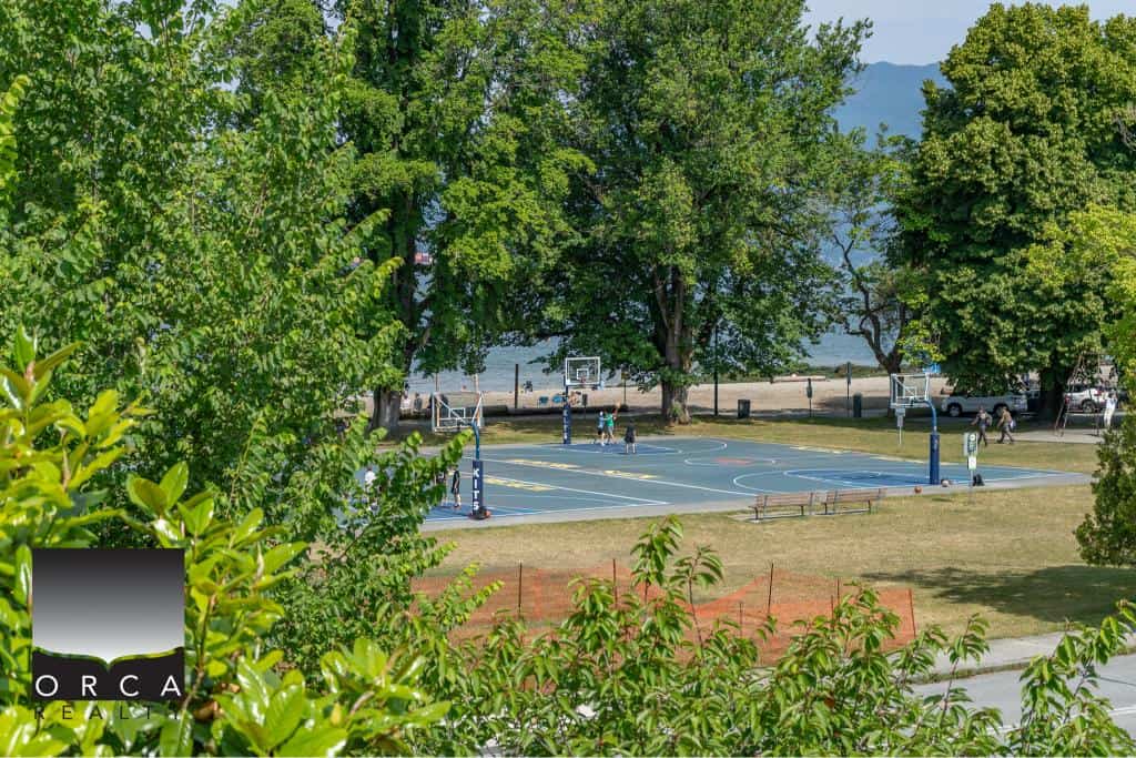 Basketball court surrounded by lush greenery near a waterfront in Orca, BC, offering ideal outdoor recreation and scenic views, perfect for local residents and visitors.