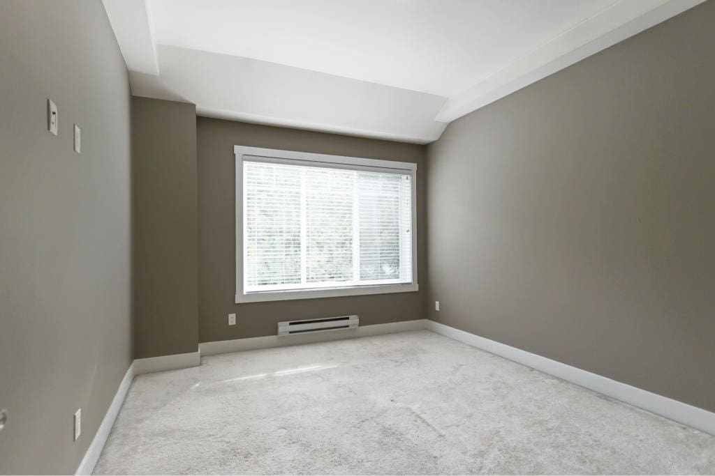 Bright empty bedroom with large window, neutral grey walls, and plush white carpet, perfect for home staging or real estate listings.