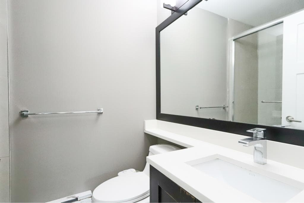 Modern bathroom with grey walls, sleek white vanity, large black-framed mirror, and contemporary fixtures showcasing Vancouver BC real estate by Orca Realty Inc.