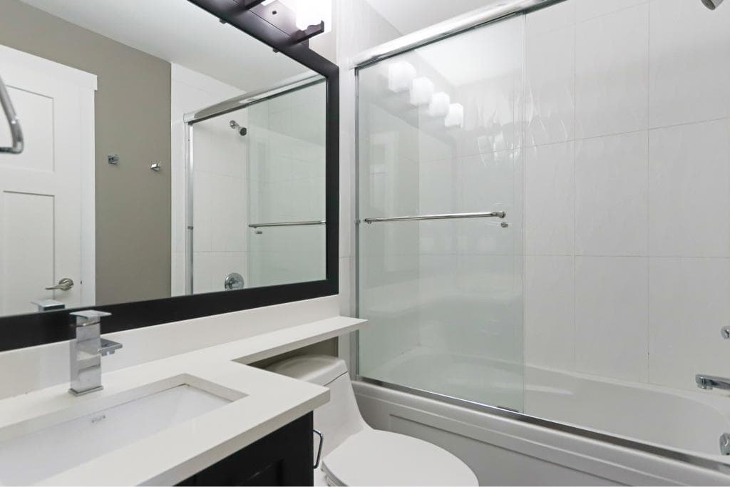 Modern bathroom with white tile walls, glass shower enclosure, and contemporary fixtures, perfect for Vancouver coastal living.