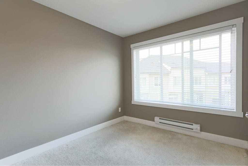 Bright empty bedroom with large window and neutral wall paint, ideal for home staging or real estate listings by Orca Realty Inc.