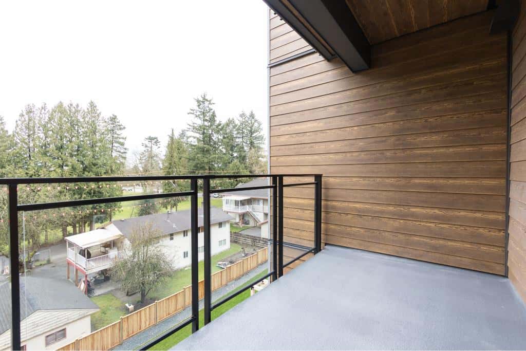 Bright balcony with modern black railing, overlooking a suburban neighbourhood with trees and residential homes in Vancouver, BC.