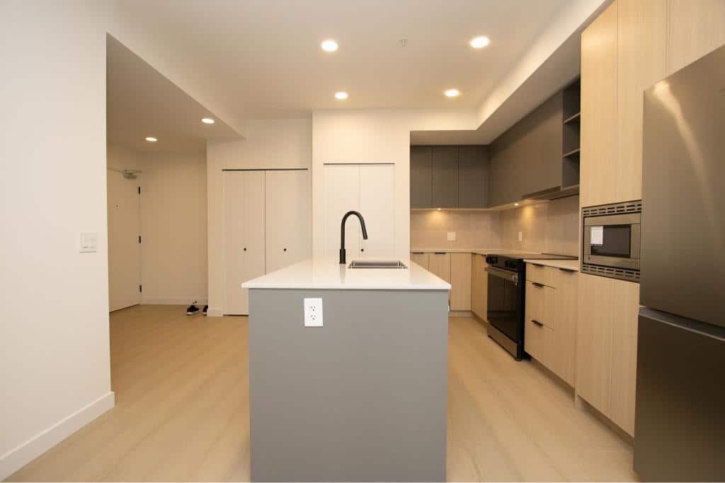 Modern open-concept kitchen with grey and natural wood cabinets, stainless steel appliances, and a central island with a black sink, ideal for Vancouver real estate listings.