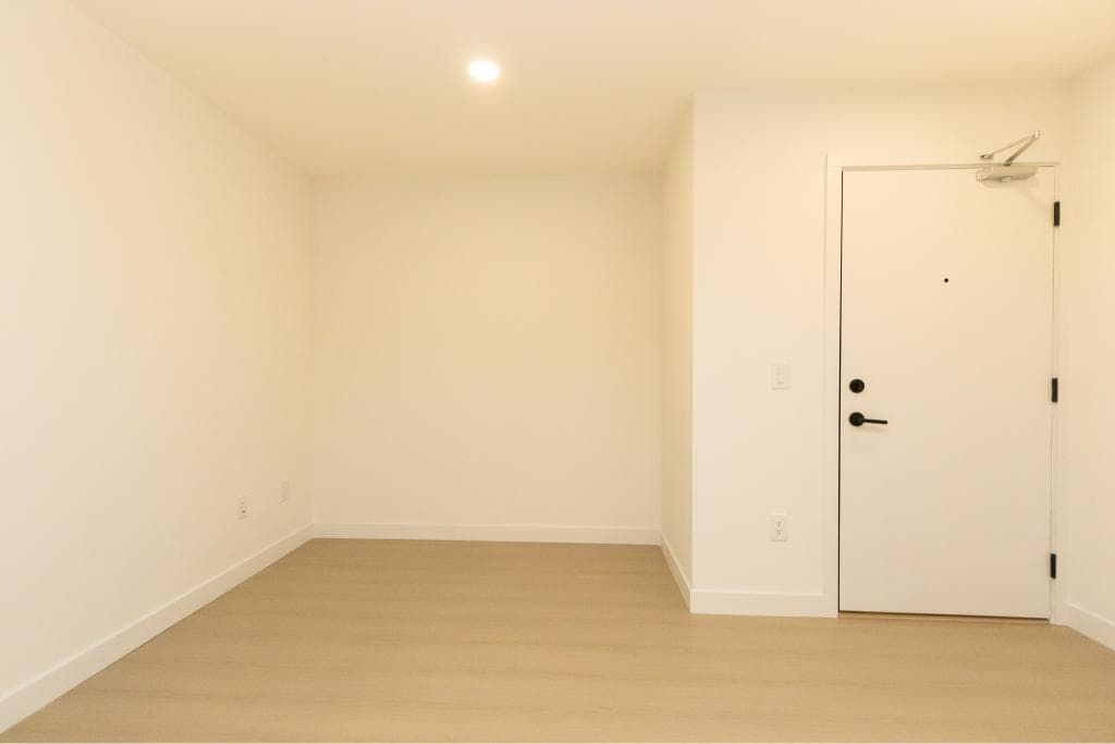 Spacious, modern empty room with white walls and light wood flooring in an Orca Realty property, showcasing contemporary interior design and ready for personalization.