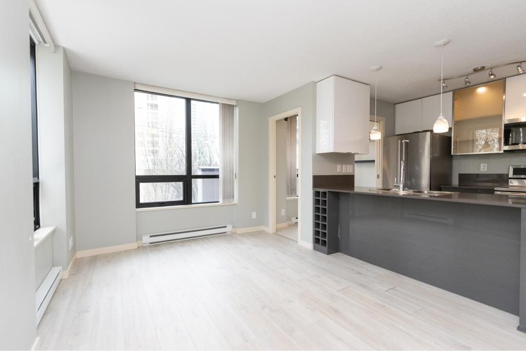 Spacious open-concept living room with large windows and modern kitchen in a Vancouver-area apartment, showcasing contemporary interior design and natural light.