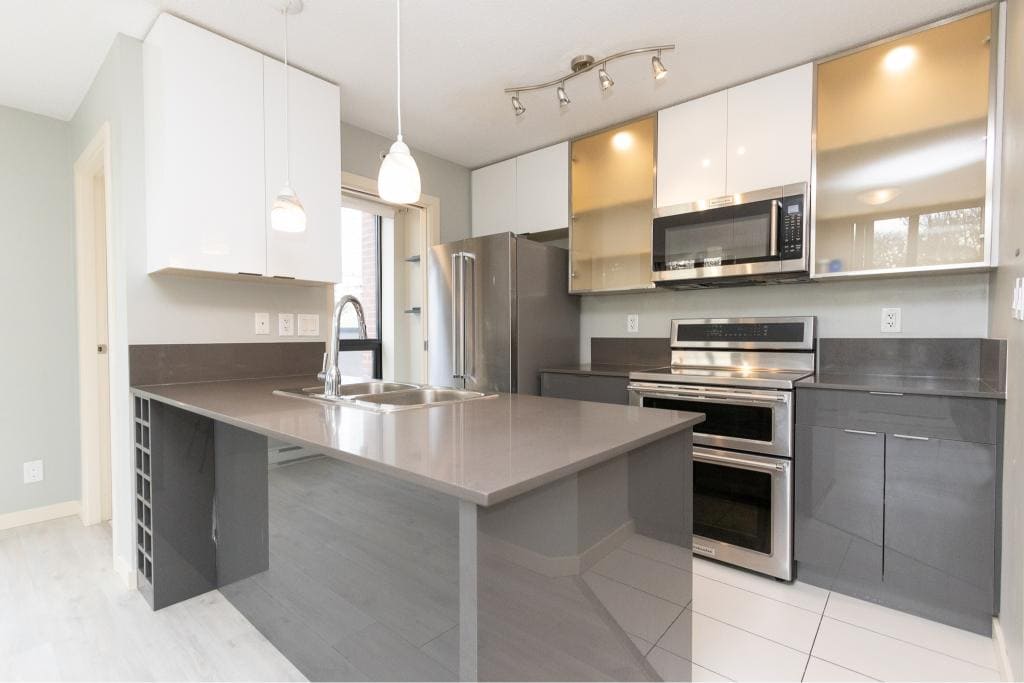 Modern kitchen with stainless steel appliances, grey cabinetry, and sleek countertops in a contemporary home by Orca Realty Inc.