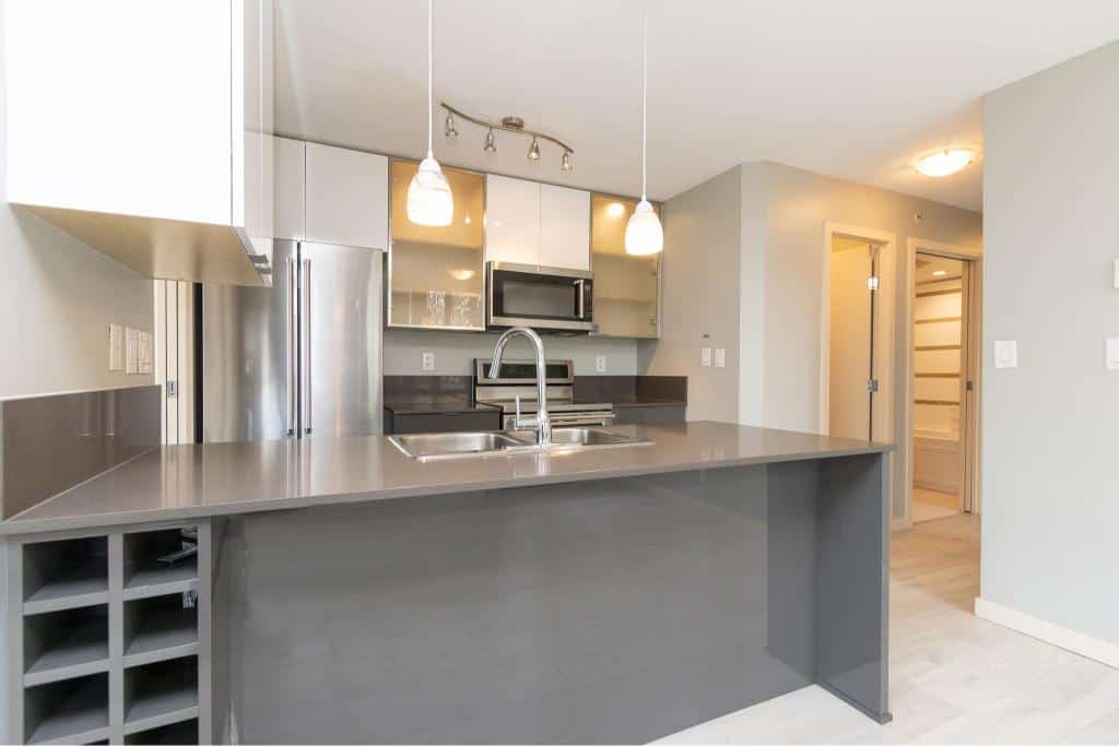 Modern kitchen interior with stainless steel appliances and minimalist design, showcasing a sleek grey countertop and contemporary lighting for upscale real estate in Vancouver.