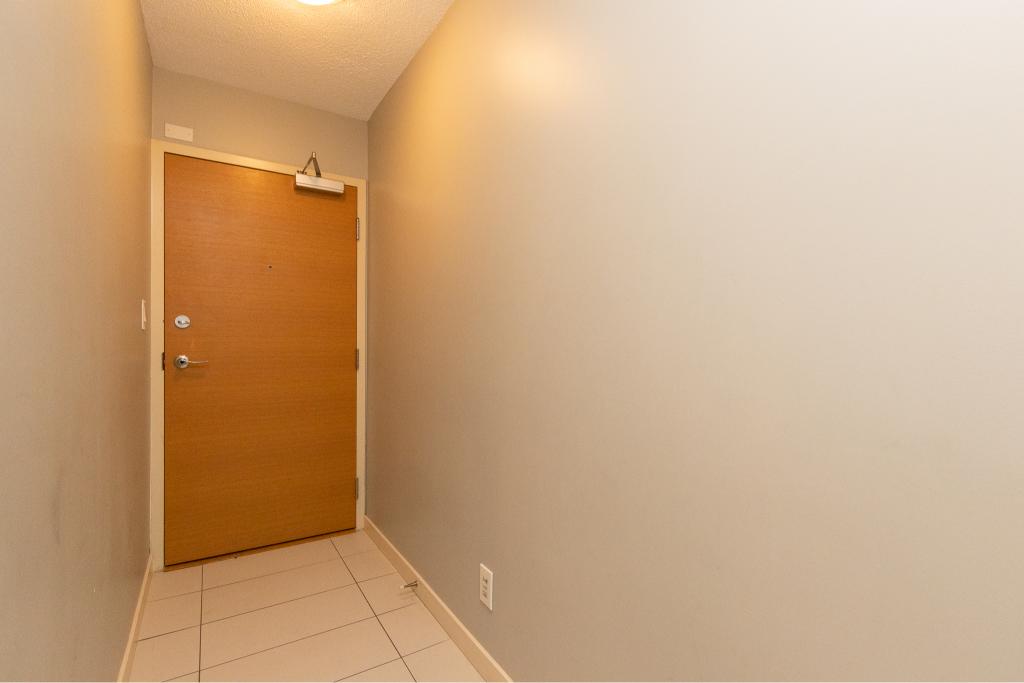 Modern residential apartment entryway with a wooden door, neutral wall colours, and tiled flooring, showcasing professional real estate presentation by Orca Realty Inc.