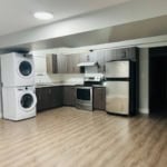 Modern kitchen with laundry appliances in Vancouver condo, featuring stainless steel fridge, stove, and wood cabinetry. Ideal for contemporary urban living and real estate investment.