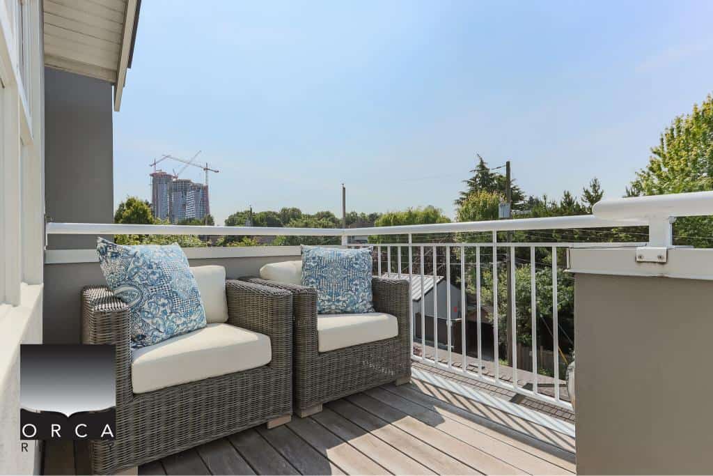 Cozy outdoor balcony with wicker sofa and decorative pillows, ideal for relaxing and enjoying city views, featuring modern design by Orca Realty Inc., Vancouver real estate experts.