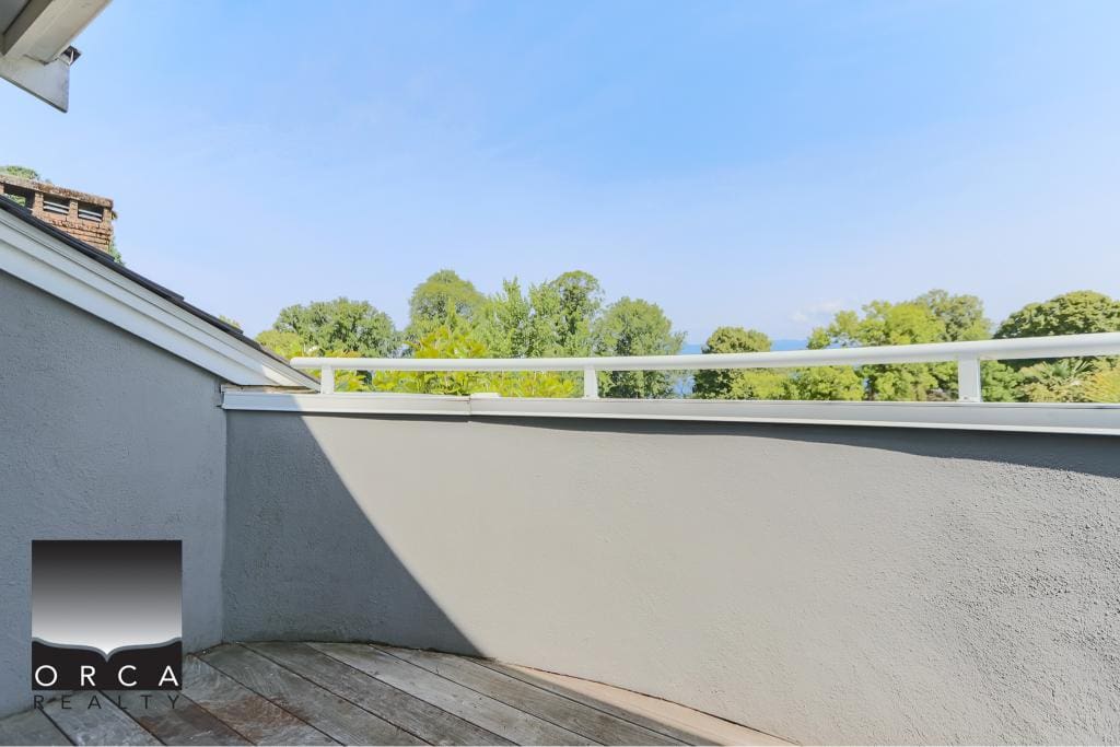 Balcony with white railing overlooking lush green trees under a clear blue sky in Vancouver, British Columbia, outdoor residential space, real estate photography, modern home balcony shot.