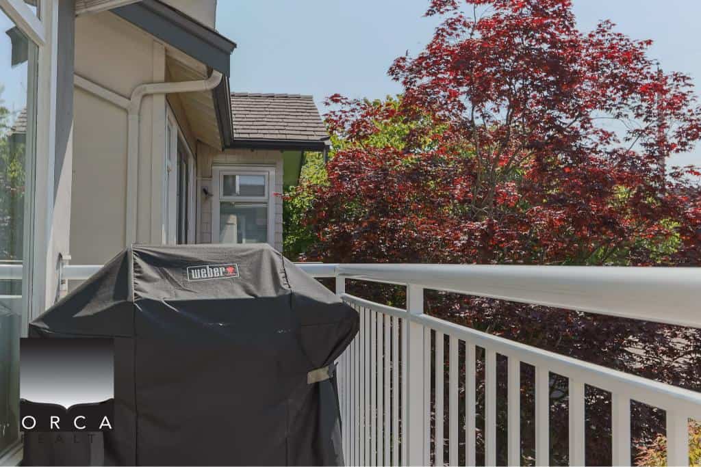 Spacious balcony with white railing and a barbecue grill, surrounded by vibrant red maple trees, offering a cozy outdoor space for relaxation and entertaining in a beautiful residential setting.