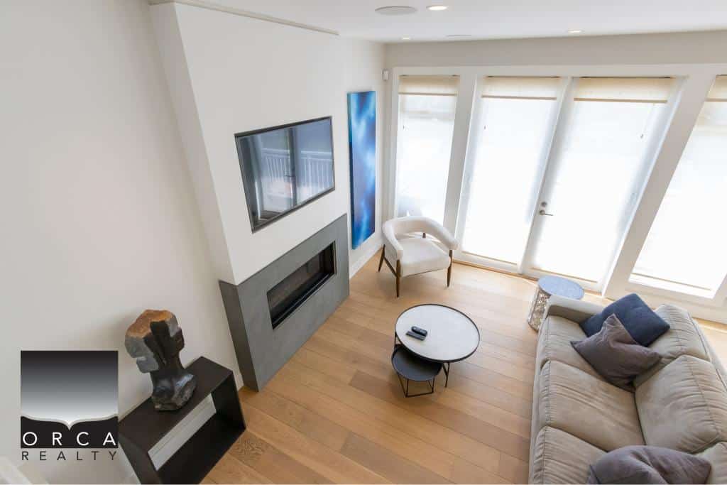 Modern living room with large windows, neutral-toned sofa, mounted flat-screen TV, and contemporary fireplace, perfect for Vancouver-area real estate showcasing.