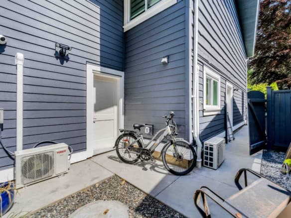Modern house exterior with blue siding, outdoor air conditioning unit, and a bicycle parked on the concrete patio, exemplifying professional real estate offerings from Orca Realty Inc.