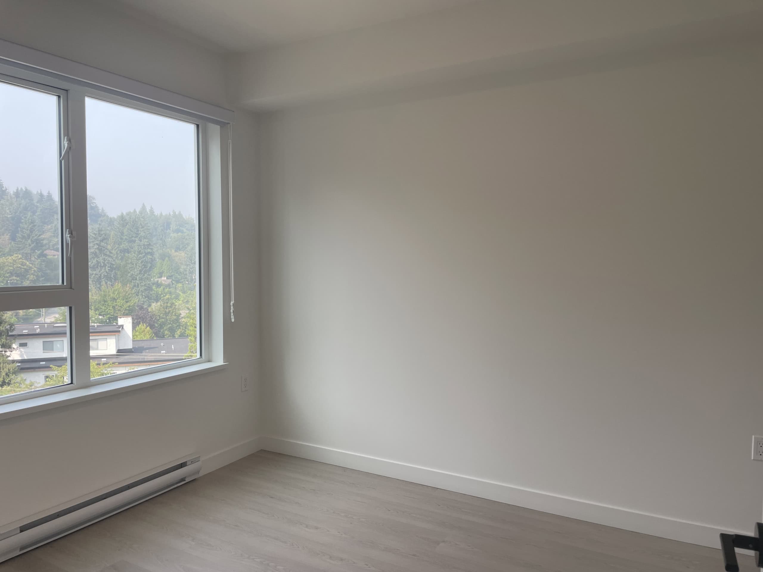 Bright empty room with large window showcasing a scenic view of trees and neighboring houses, ideal for real estate listings and property showcasing by Orca Realty Inc.