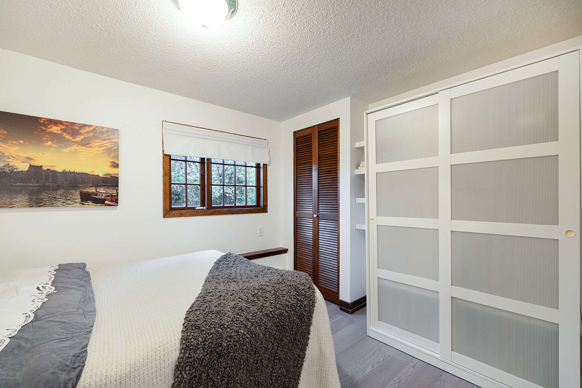 Cozy bedroom with white walls, wooden window frame, and a white sliding closet door, featuring natural light and simple decor, ideal for showcasing Vancouver Island homes.