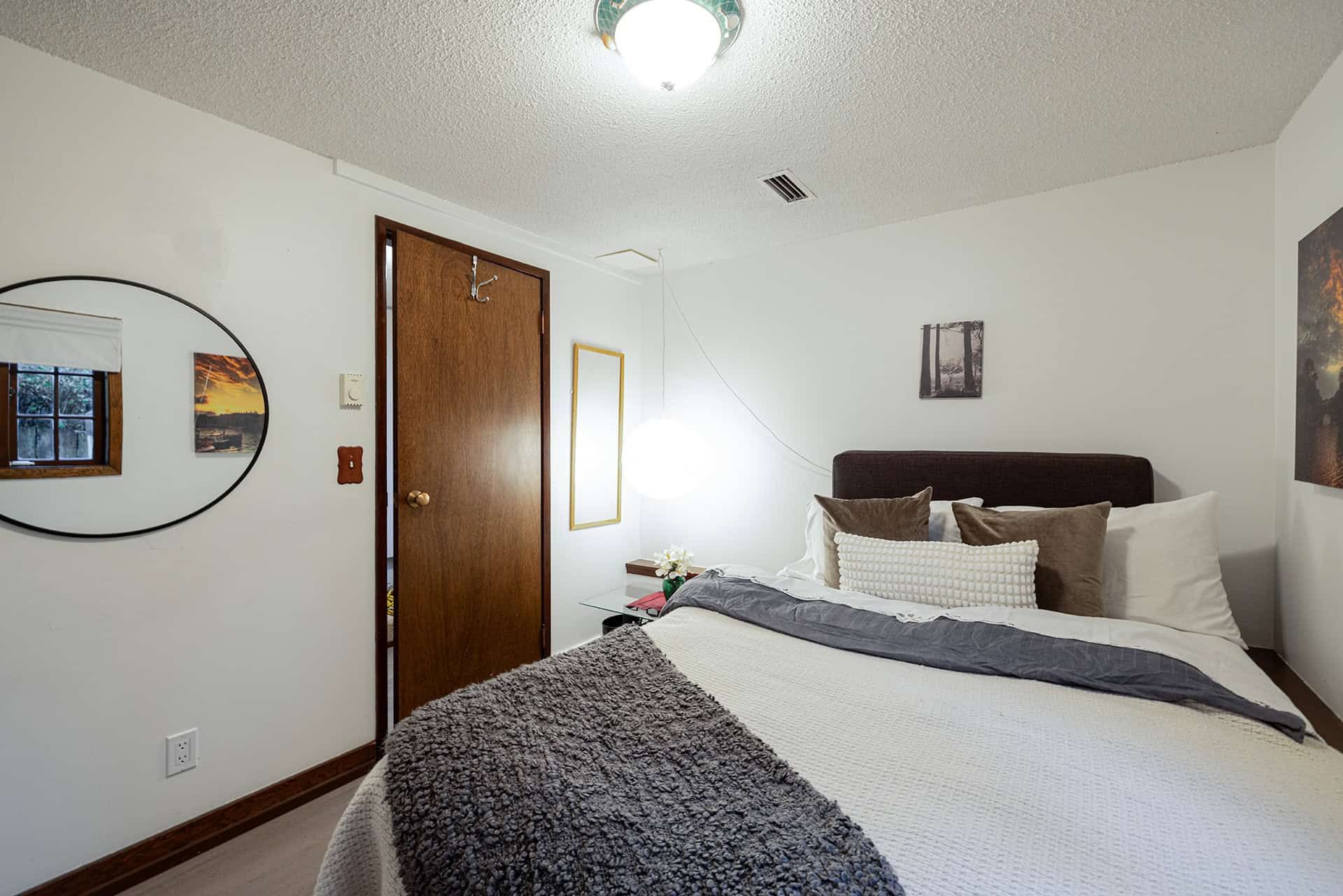 Cozy bedroom with white walls, wooden door, modern lighting, and neatly made bed with decorative pillows, ideal for Vancouver homebuyers seeking peaceful residential spaces.